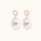 Gold-plated drop earrings with iridescent baroque pearls and crystal flower accents on cream background