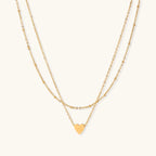 Delicate double-chain gold necklace with tiny heart pendant on cream background