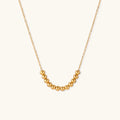 Delicate gold-plated necklace with graduated spherical beads forming gentle smile curve on beige background