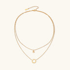 Gold layered necklace set with sunburst and smiley face pendants on delicate chains against white background.
