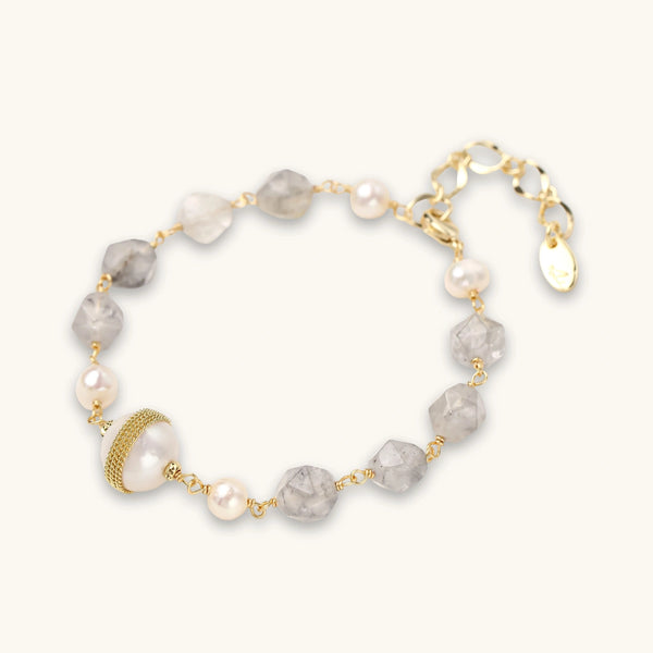 Bracelet with cloudy quartz beads, freshwater pearls, and gold-wrapped baroque pearl centerpiece on white background.