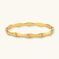 Gold-toned wavy bangle with bamboo-style segments and CZ crystal clusters on cream background. 18K plated stainless steel.