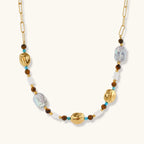 Gold-plated beaded necklace with iridescent baroque pearls, turquoise stones, and brown natural beads on neutral background.