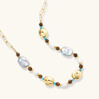 Gold-plated beaded necklace with iridescent baroque pearls, turquoise stones, and brown natural beads on neutral background.