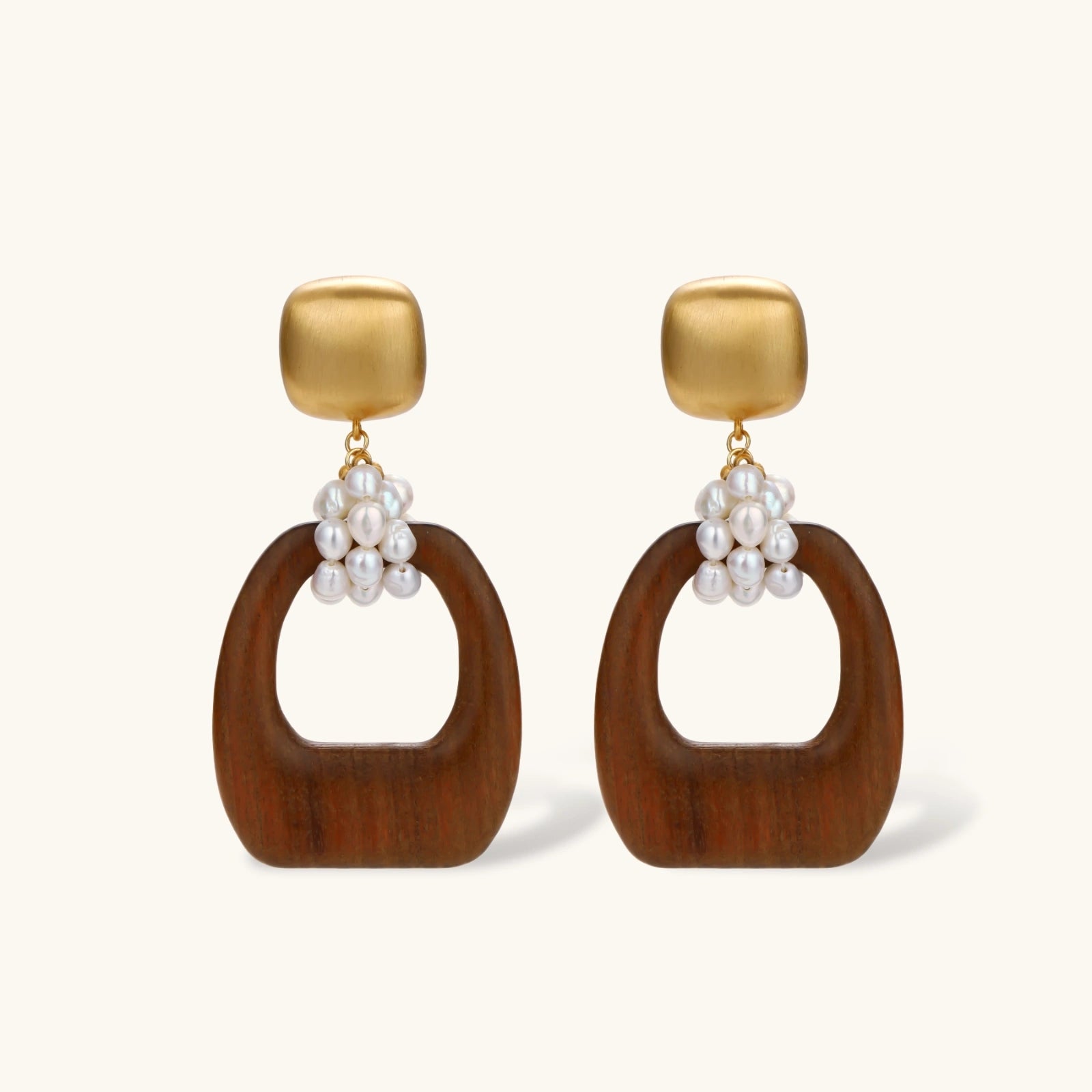 Gold-plated stud earrings with pearl clusters and organic brown wooden hoops on cream background