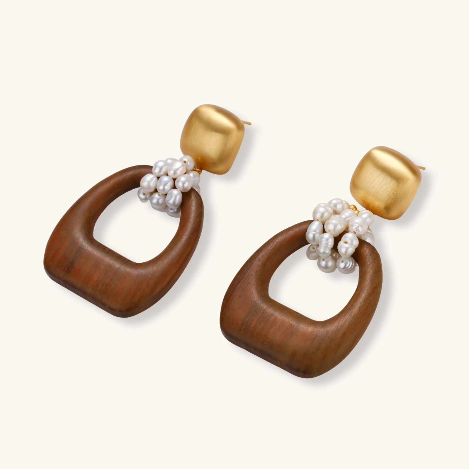 Gold-plated stud earrings with pearl clusters and organic brown wooden hoops on cream background