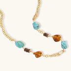Statement necklace with gold chain, turquoise stones, amber beads, and wooden elements on cream background.