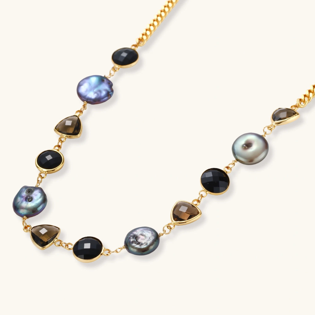 18k gold-plated chain necklace featuring lustrous baroque pearls, black onyx rounds, and smoky quartz triangular stones on white background.