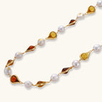 Gold-plated copper necklace with amber teardrop settings and white baroque freshwater pearls on cream background.