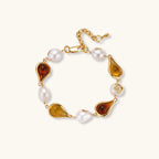 Elegant bracelet with alternating baroque pearls and amber teardrop gemstones set in 18k gold-plated copper on cream background.