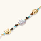 Gold-plated bracelet with baroque pearl centerpiece, turquoise and amber natural stones on adjustable chain against white background.